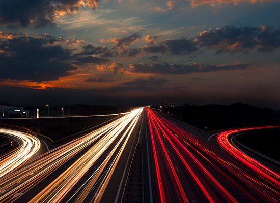 Landscape view of highway with red and white streaks on road and sunset with clouds